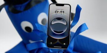 نمای جلوی یک آیفون با تاریخ اول آوریل که توسط یک عروسک بادی آبی رنگ نگه داشته شده است.