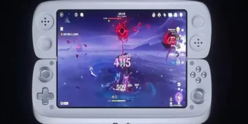 کنسول بازی دستی سفید در حال اجرای بازی Genshin Impact با افکت‌های رزمی قرمز.