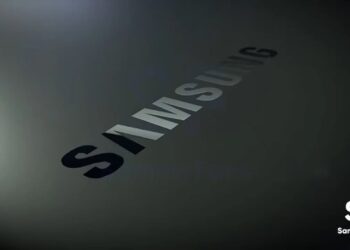 نمای نزدیک و زاویه‌دار از لوگوی نوشتاری سامسونگ با بافت تیره و براق روی یک سطح خاکستری.