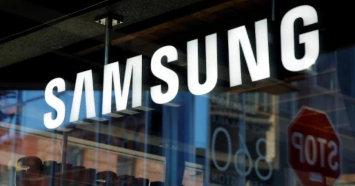 نمای نزدیک از تابلو و لوگوی سفید Samsung نصب‌شده روی شیشه ویترین یک فروشگاه، با انعکاس محیط شهری در پس‌زمینه
