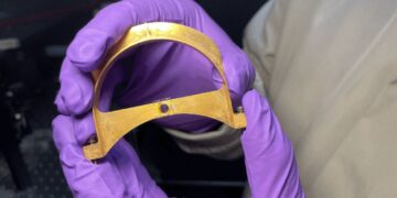 گاه نزدیک به قطعه فلزی U-شکل با تراشه نانویی نصب‌شده روی پایه مرکزی در دست پژوهشگر با دستکش بنفش