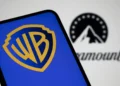 نمای نزدیک از صفحهنمایش گوشی هوشمند با نمایش لوگوی Warner Bros (WB) در رنگ آبی و زرد؛ در پسزمینه تار، لوگوی Paramount بهصورت خارج از فوکوس قابل مشاهده است.