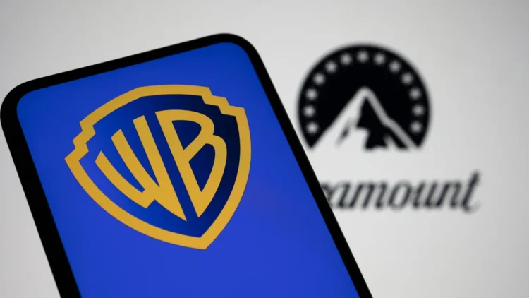 نمای نزدیک از صفحه‌نمایش گوشی هوشمند با نمایش لوگوی Warner Bros (WB) در رنگ آبی و زرد؛ در پس‌زمینه تار، لوگوی Paramount به‌صورت خارج از فوکوس قابل مشاهده است.
