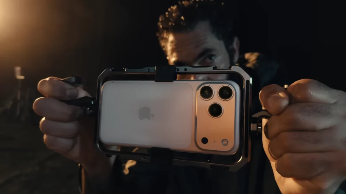 نمای نزدیک از Apple iPhone 17 Pro / Pro Max نصبشده روی camera rig حرفهای فیلمبرداری موبایل؛ بدنه پشتی روشن با لوگوی اپل، ماژول دوربین چندگانه بزرگ با لنزهای برجسته، فریم فلزی محافظ، دستگیرههای دوطرفه و نورپردازی سینمایی کمنور که بر کاربرد ویدیوگرافی حرفهای تأکید دارد.