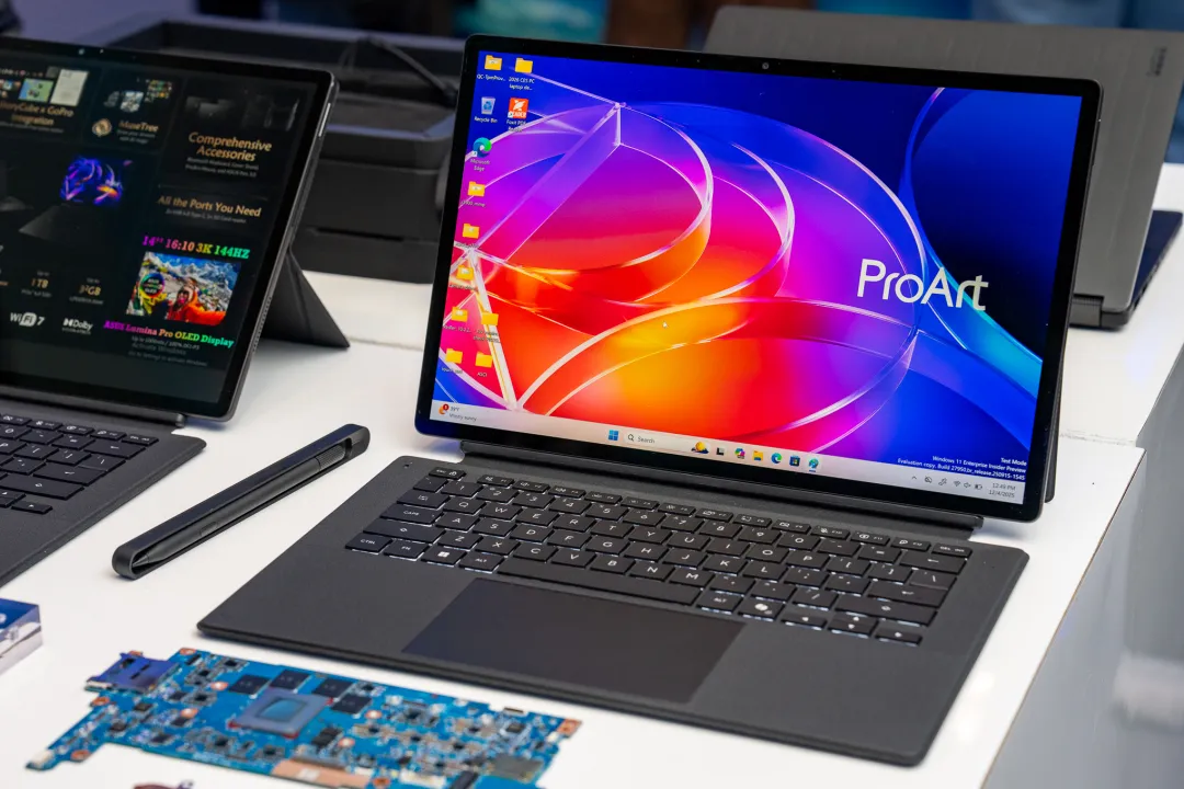 لپ‌تاپ ASUS ProArt PZ13 با کیبورد جداشونده و قلم لمسی در کنار قطعات سخت‌افزاری روی میز.