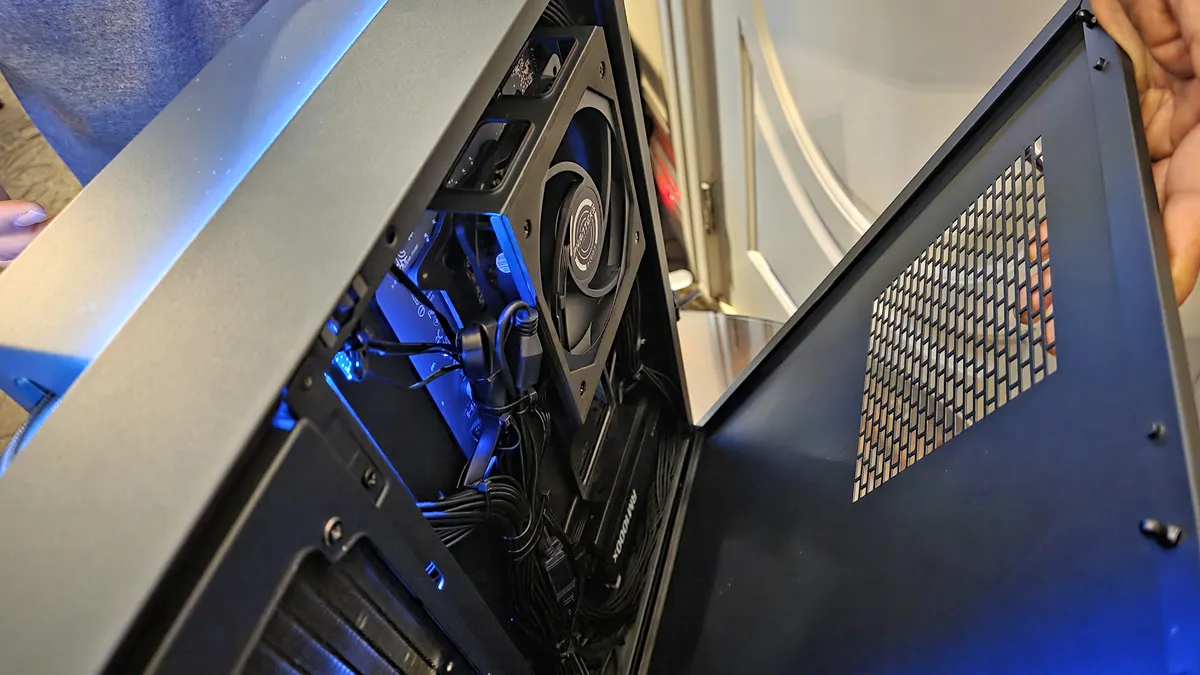 نمای درونی از یک کیس کامپیوتر مفهومی با طراحی ماژولار لایه‌ای، شامل پنل‌های مشکی مات، نورپردازی خطی LED آبی، پنل شیشه‌ای شفاف برای نمایش قطعات داخلی و فن‌های RGB؛ قرارگرفته روی میز نمایشگاهی با کارت مشخصات محصول.