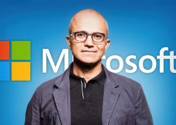 پرتره ساتیا نادلا، مدیرعامل مایکروسافت، در مقابل لوگوی بزرگ این شرکت با پس‌زمینه آبی.