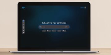 یک لپ‌تاپ باز روی میز چوبی که صفحه اصلی دستیار هوشمند جدید آمازون (Alexa.com) را نمایش می‌دهد.