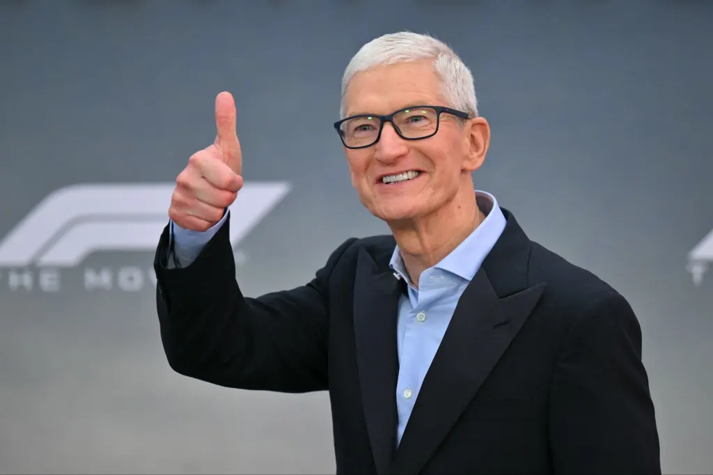 تیم کوک با کت و شلوار در یک محیط عمومی در حال نشان دادن علامت پیروزی