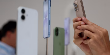 نمای نزدیک از چندین گوشی آیفون در رنگهای مختلف که روی پایههای نمایش در یک فروشگاه قرار دارند.