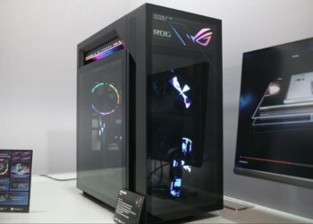 نمای زاویهدار از کیس گیمینگ مشکی ایسوس با پنل شیشهای و افکتهای هولوگرافیک روی بدنه.