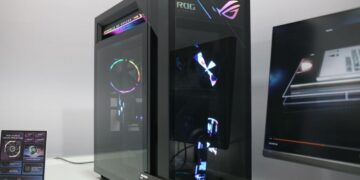 نمای زاویه‌دار از کیس گیمینگ مشکی ایسوس با پنل شیشه‌ای و افکت‌های هولوگرافیک روی بدنه.