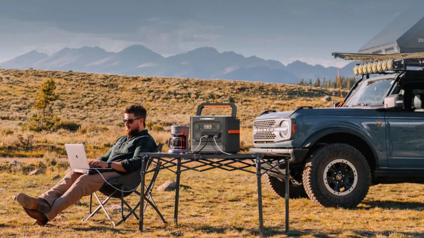 فردی در حال کار با لپتاپ در طبیعت که از ایستگاه قدرت قابل حمل Jackery Explorer 1500 برای تامین برق استفاده میکند.