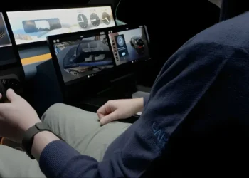 شخصی که در یک محیط شبیه‌سازی شده نشسته و چندین نمایشگر دیجیتال شناور (شامل نقشه و موسیقی) در مقابل او قرار دارد.