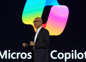 ساتیا نادلا، مدیرعامل مایکروسافت، در حال سخنرانی روی صحنه مقابل لوگوی بزرگ و رنگارنگ Microsoft Copilot.