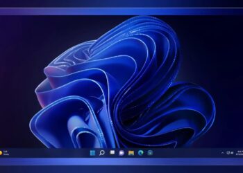 تصویر پسزمینه پیشفرض آبی رنگ ویندوز ۱۱ (Bloom) به همراه نوار وظیفه (Taskbar) در پایین که آیکونهای اپلیکیشنها در مرکز آن قرار دارند.