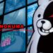اسکرین‌شات از رابط کاربری بازی Danganronpa، نمایش نمای نزدیکی از عروسک خرس سیاه و سفید Monokuma در سمت راست، و متن MONOKUMA با فونت قرمز، در مقابل دیواری از مانیتورهای کوچک نمایشگر محیط داخلی و خارجی.
