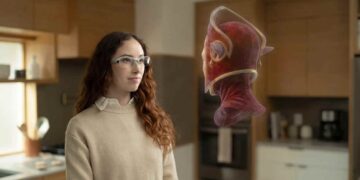 زنی با عینک واقعیت افزوده شفاف در حال تماشای یک آواتار سهبعدی شناور در آشپزخانه.