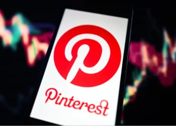 گوشی هوشمندی که لوگوی پینترست را نشان می‌دهد و در پس‌زمینه آن نمودارهای بورس و بازارهای مالی دیده می‌شود.