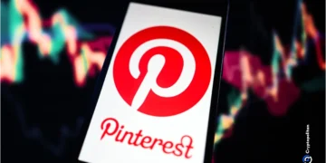 گوشی هوشمندی که لوگوی پینترست را نشان می‌دهد و در پس‌زمینه آن نمودارهای بورس و بازارهای مالی دیده می‌شود.