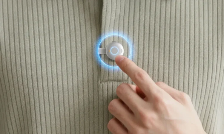 نمای نزدیک از فشار دادن دکمه یک دستگاه ضبط صدای کوچک و دایرهای که روی یقه لباس نصب شده است.