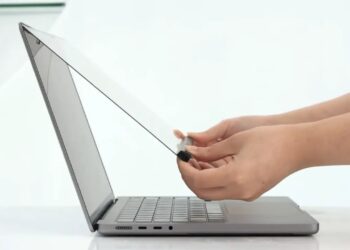 نمایی از کنار که نحوه نصب یک لایهی محافظ شفاف یا اکسسوری لمسی را روی صفحه نمایش لپتاپ MacBook نشان میدهد.