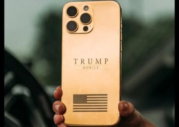 نمای پشت گوشی هوشمند با بدنه طلایی براق، لوگوی متنی TRUMP MOBILE در مرکز، ماژول دوربین مربعی با چهار دهانه لنز در گوشه بالا و نماد پرچم ایالات متحده در بخش پایینی بدنه