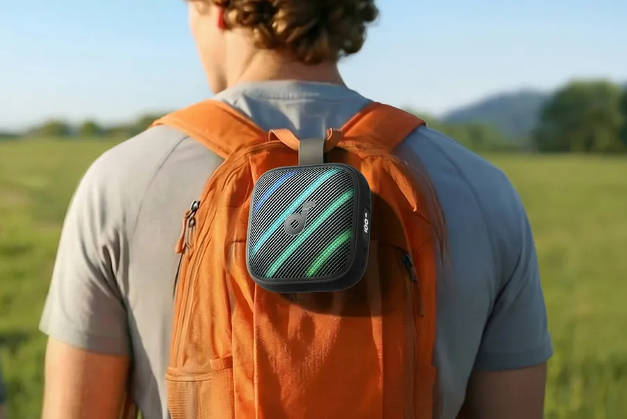 اسپیکر بلوتوثی کوچک و مشکی انکر با نورپردازی RGB که به بند یک کوله‌پشتی نارنجی در طبیعت متصل شده است.