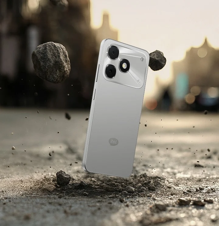 گوشی هوشمند itel نقرهای در حال سقوط روی زمین خاکی و برخورد با سنگها.