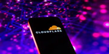 تصویر مفهومی از یک تلفن هوشمند با نمایش لوگوی Cloudflare روی صفحهنمایش. پسزمینه شامل شبکهای انتزاعی از نقاط و خطوط نورانی به رنگهای بنفش و آبی است که مفاهیم زیرساخت شبکه، امنیت ابری و ترافیک داده را القا میکند.