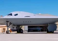 نمای روبه‌روی بمب‌افکن رادارگریز B-21 Raider در داخل آشیانه با پرچم بزرگ ایالات متحده در پس‌زمینه