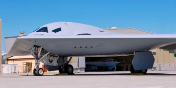 نمای روبهروی بمبافکن رادارگریز B-21 Raider در داخل آشیانه با پرچم بزرگ ایالات متحده در پسزمینه