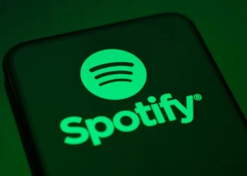 لوگوی Spotify با نماد دایره‌ای سبزرنگ و خطوط صوتی، نمایش‌داده‌شده روی صفحه یک گوشی هوشمند با پس‌زمینه تیره، که هویت بصری سرویس استریم موسیقی اسپاتیفای را برجسته می‌کند.