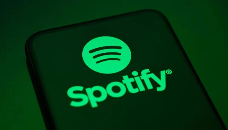 لوگوی Spotify با نماد دایره‌ای سبزرنگ و خطوط صوتی، نمایش‌داده‌شده روی صفحه یک گوشی هوشمند با پس‌زمینه تیره، که هویت بصری سرویس استریم موسیقی اسپاتیفای را برجسته می‌کند.