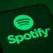 لوگوی Spotify با نماد دایره‌ای سبزرنگ و خطوط صوتی، نمایش‌داده‌شده روی صفحه یک گوشی هوشمند با پس‌زمینه تیره، که هویت بصری سرویس استریم موسیقی اسپاتیفای را برجسته می‌کند.
