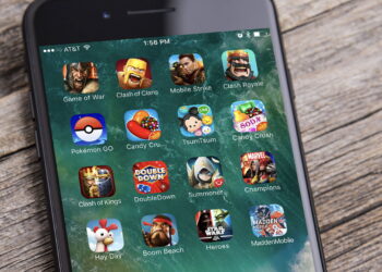 نمای نزدیک از صفحه یک گوشی هوشمند که مجموعه‌ای از آیکن بازی‌های موبایلی محبوب مانند Pokémon GO، Clash of Clans، Candy Crush، Hay Day و Madden Mobile را در قالب یک پوشه روی صفحه‌نمایش نشان می‌دهد.