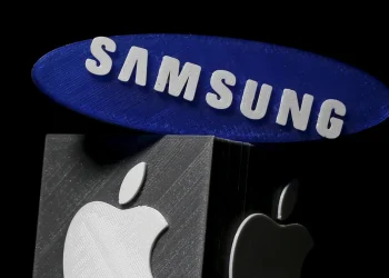 نمای مفهومی از لوگوهای Samsung و Apple که به‌صورت نمادین روی سازه‌های سه‌بعدی در پس‌زمینه تیره قرار گرفته‌اند؛ تصویری که به رقابت و هم‌زیستی دو برند بزرگ فناوری در بازار جهانی اشاره دارد.