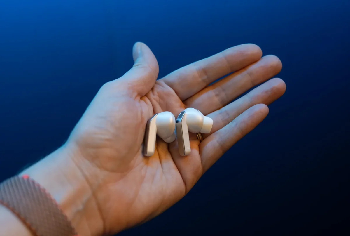 دو عدد ایرباد گلکسی بادز ۴ با بدنه نقره‌ای و طراحی پایه‌دار (Stem) در کف دست انسان.