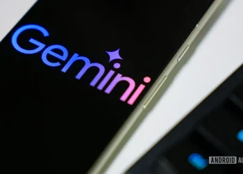 نمای نزدیک از لوگوی رنگارنگ Gemini گوگل بر روی صفحه نمایش یک گوشی هوشمند در کنار لبه کیبورد.