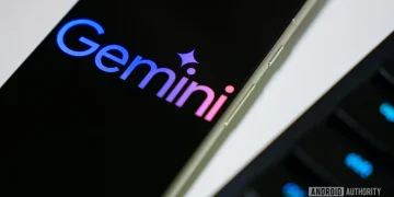 نمای نزدیک از لوگوی رنگارنگ Gemini گوگل بر روی صفحه نمایش یک گوشی هوشمند در کنار لبه کیبورد.