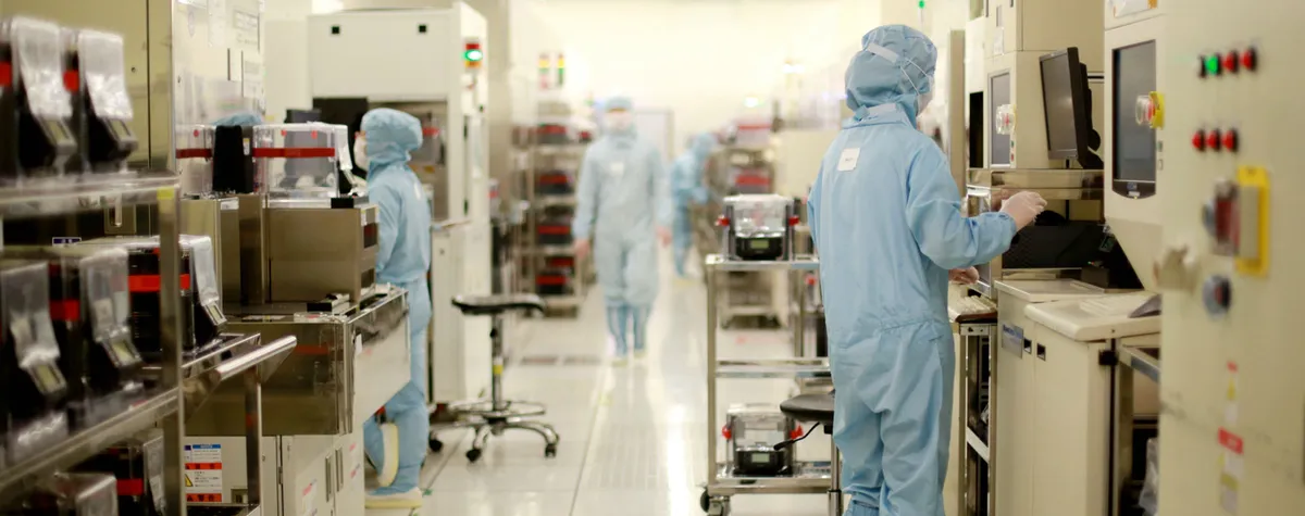 تکنسین‌ها با لباس‌های مخصوص محافظ (اتاق تمیز) در حال کار با تجهیزات پیشرفته در یک کارخانه تولید تراشه.