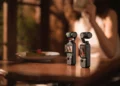 دو دوربین کوچک DJI Osmo Pocket 3 روی یک میز چوبی در محیطی با نور گرم و دنج.