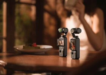 دو دوربین کوچک DJI Osmo Pocket 3 روی یک میز چوبی در محیطی با نور گرم و دنج.