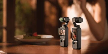دو دوربین کوچک DJI Osmo Pocket 3 روی یک میز چوبی در محیطی با نور گرم و دنج.