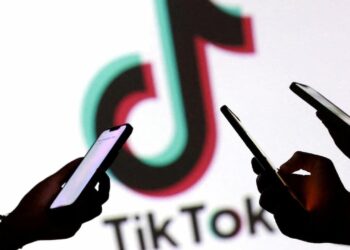 سیلوئت دست‌های چندین نفر که در حال کار با گوشی هوشمند در مقابل لوگوی بزرگ تیک‌تاک هستند.