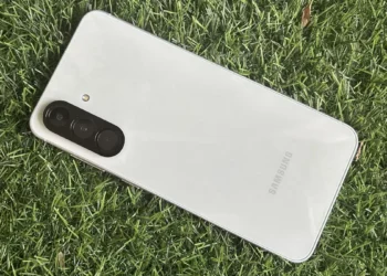 نمای واقعی از پشت گوشی Samsung Galaxy A56 با بدنه روشن، ماژول دوربین سه‌گانه عمودی و فریم تخت که روی سطح چمن قرار گرفته و جزئیات طراحی فیزیکی دستگاه را نمایش می‌دهد.
