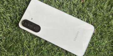 نمای واقعی از پشت گوشی Samsung Galaxy A56 با بدنه روشن، ماژول دوربین سه‌گانه عمودی و فریم تخت که روی سطح چمن قرار گرفته و جزئیات طراحی فیزیکی دستگاه را نمایش می‌دهد.