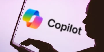 نمای نزدیک از صفحه‌نمایش یک لپ‌تاپ که لوگوی Microsoft Copilot با آیکن گرادینتی رنگین‌کمانی و متن Copilot روی پس‌زمینه روشن نمایش داده شده است. تصویر به استفاده از دستیار هوش مصنوعی Copilot در محیط کاری و تعامل کاربر با ابزارهای AI مایکروسافت اشاره دارد.