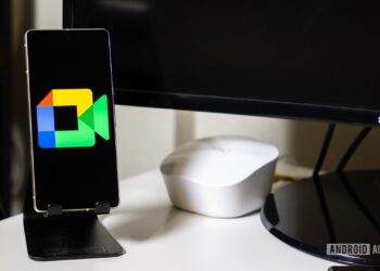 گوشی هوشمندی روی پایه که لوگوی رنگی Google Meet را در کنار یک مانیتور سامسونگ نشان می‌دهد.