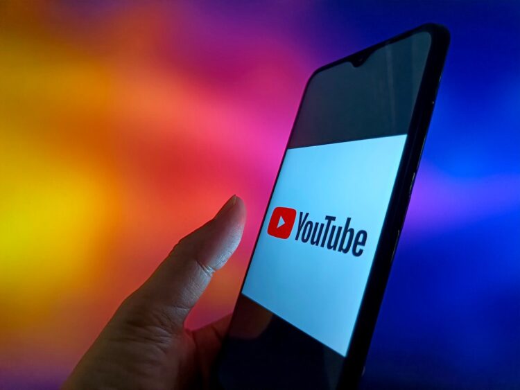 نمای نزدیک از گوشی هوشمندی که لوگوی یوتیوب را در یک پس‌زمینه رنگی و پرنور نشان می‌دهد.